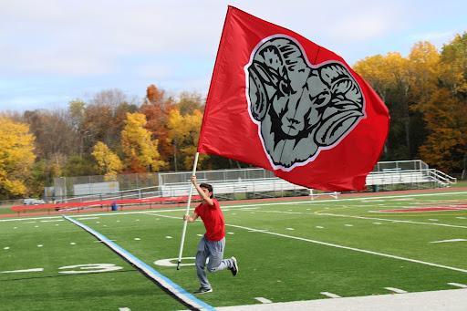 Photo shows senior Ian McIntyre waving a Red Rams flag at a pep rally. Photo Credit: jamesvilledewitt.org